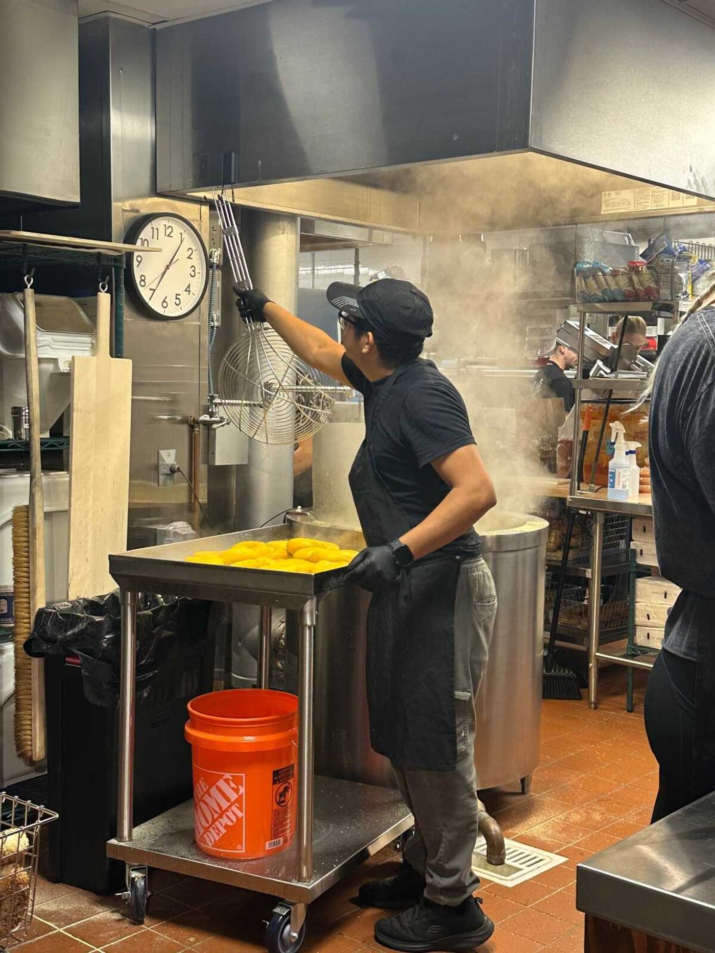A cook at Shug’s Bagels lifts kettle-boiled bagels from a steaming vat in the open kitchen