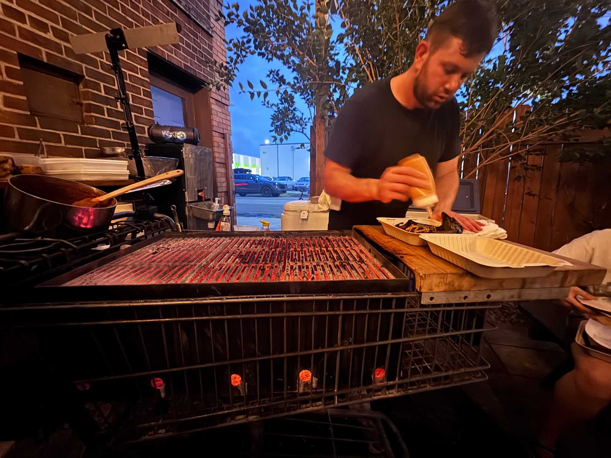 Chef Andrew Stevick plating from a shopping-cart charcoal grill at dusk
