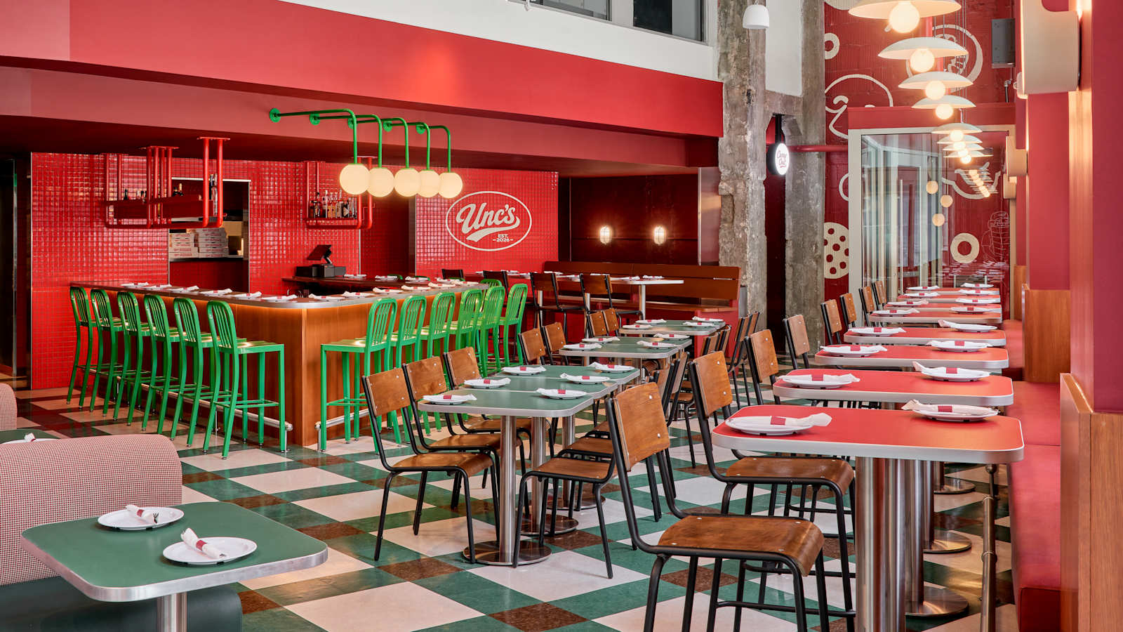 The dining room at Unc’s Pizza in Capitol Park: red walls, green stools, checkered floor, and the Unc’s oval on the tile