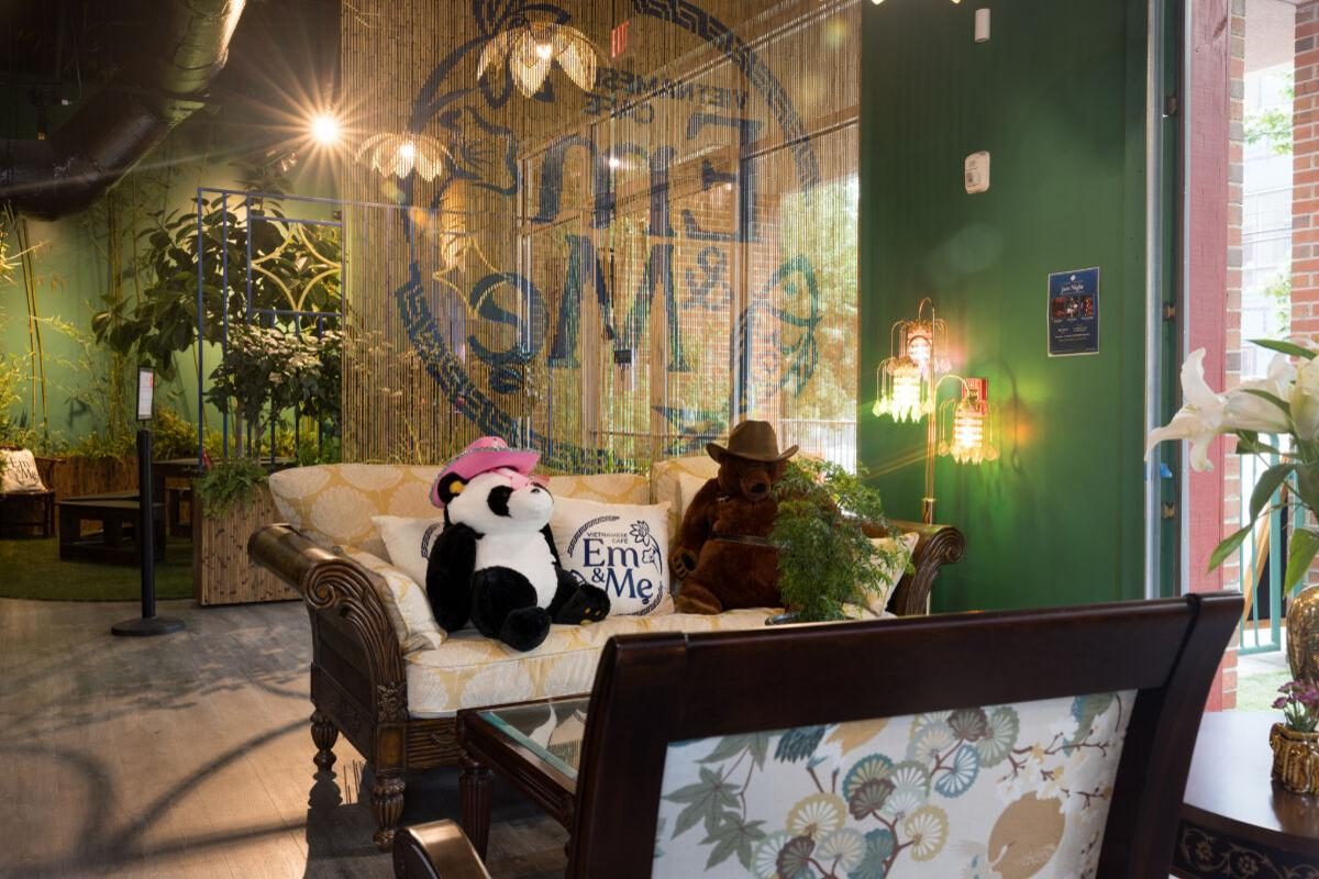Inside Em and Mẹ in Germantown: carved sofa, plants, and the cafe’s tiger emblem on a beaded curtain