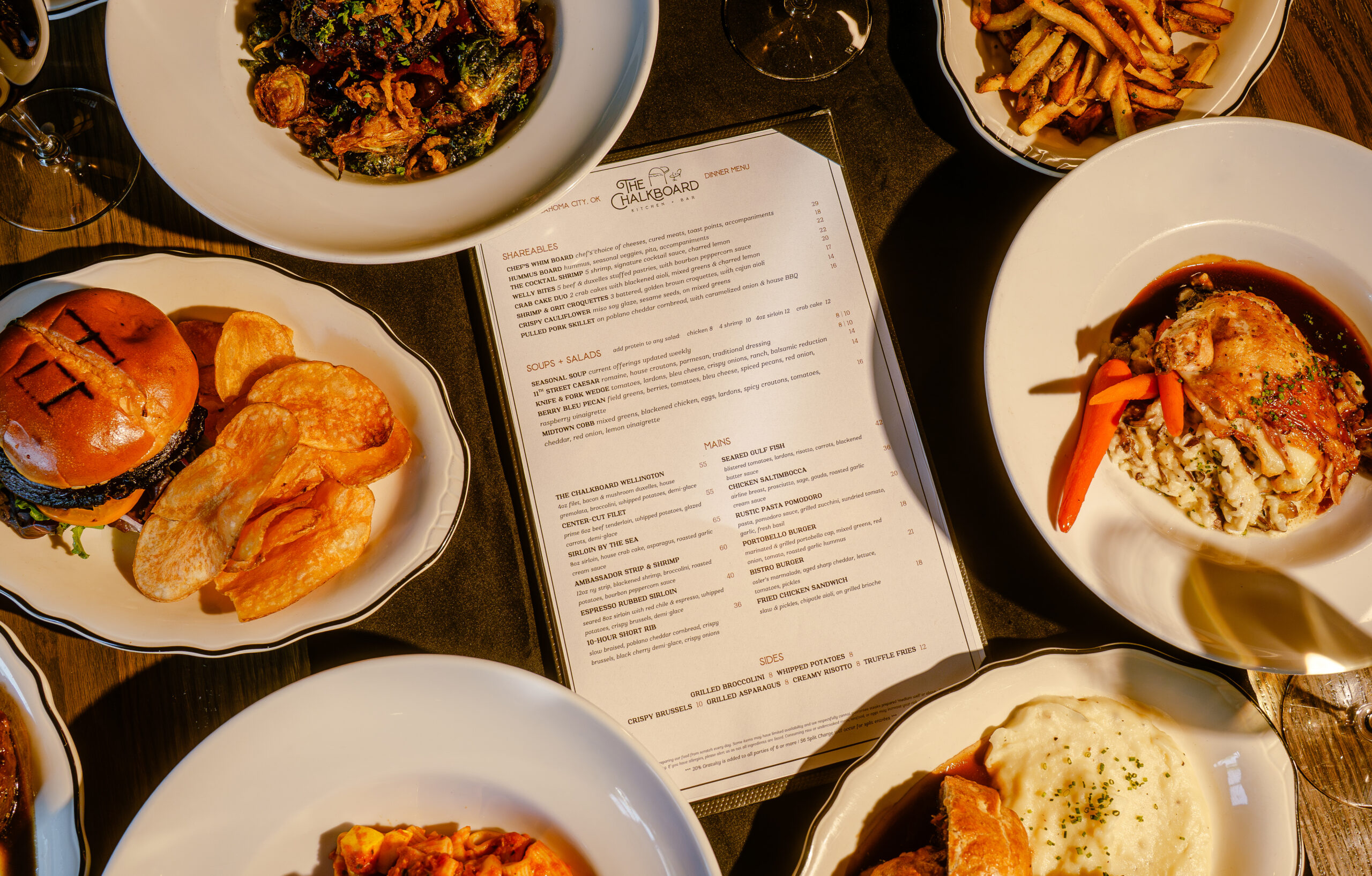 Overhead dinner spread at The Chalkboard Kitchen + Bar: Wellington, pasta, burger, fries, and the printed dinner menu