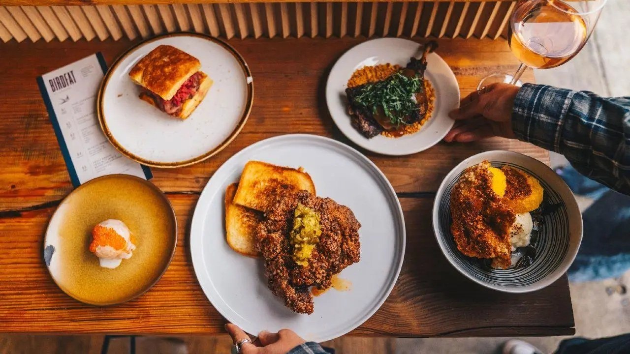 A spread of Birdfat dishes on a wooden table, including fried chicken and a menu card