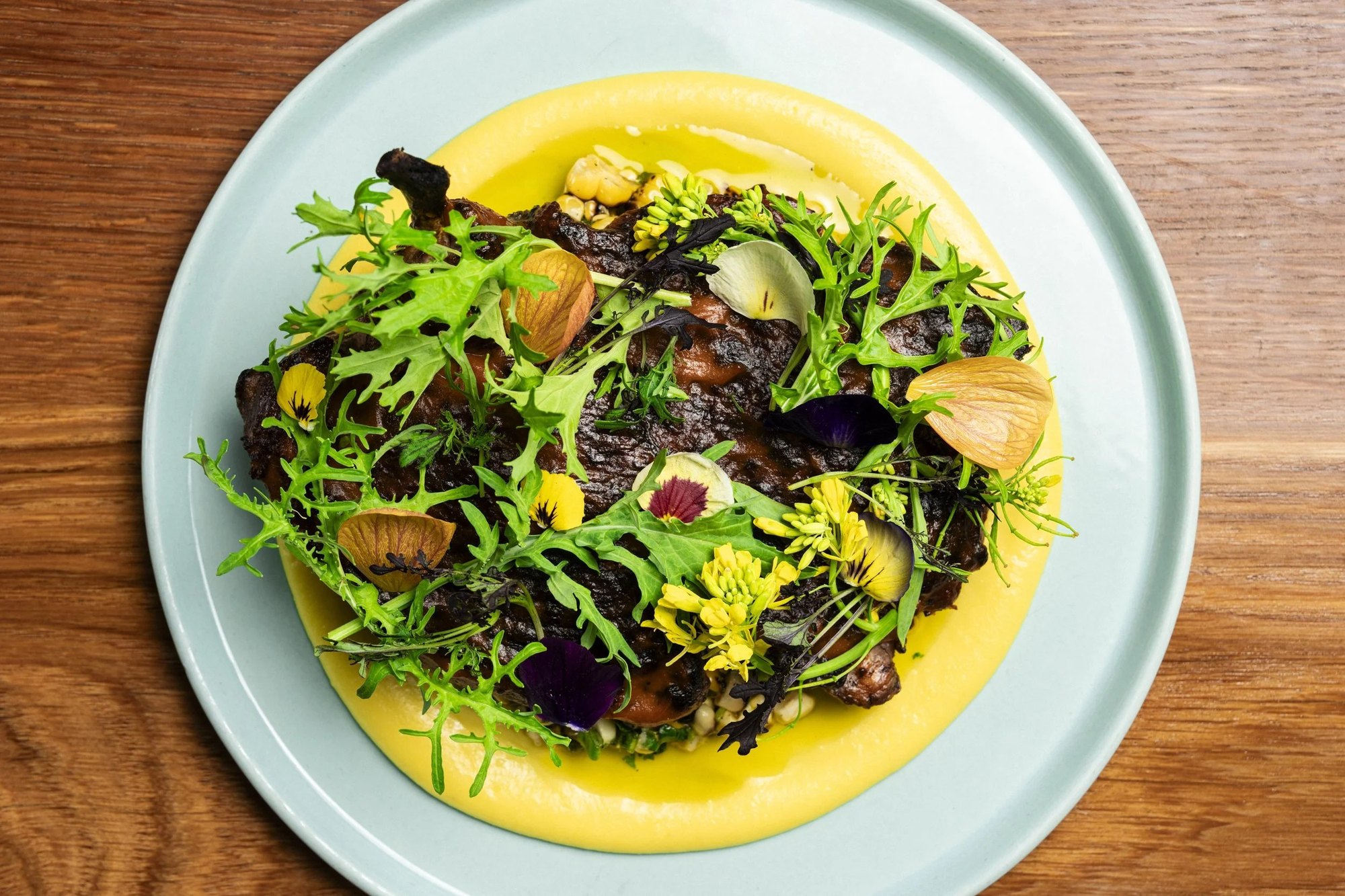 A plated dish at Kann: charred protein on a yellow purée with herbs and edible flowers