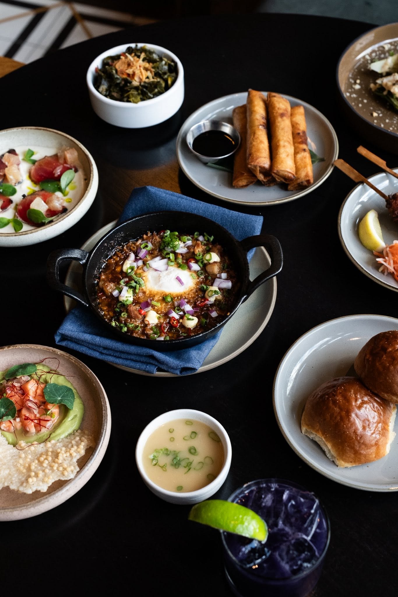 A Pamana dinner spread: sisig with egg, lumpia, crudo, and a purple cocktail