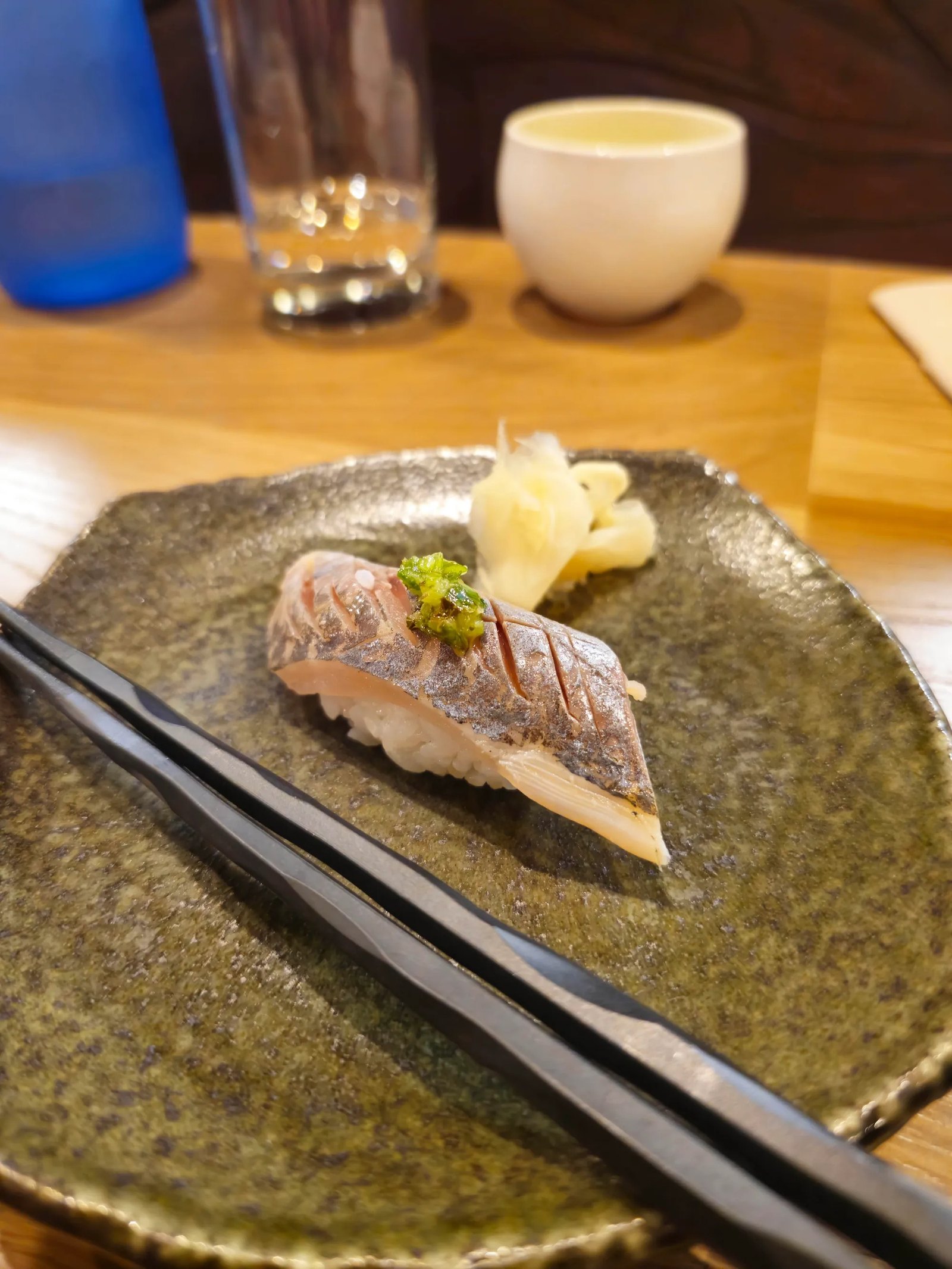Aji nigiri on a rustic plate at Sazanami, with pickled ginger and chopsticks