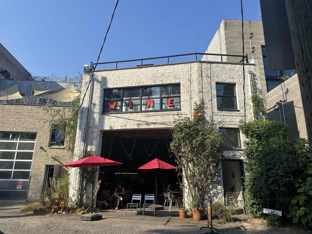 Imperfetta wine bar in Fremont: a concrete warehouse with the garage door up and red patio umbrellas